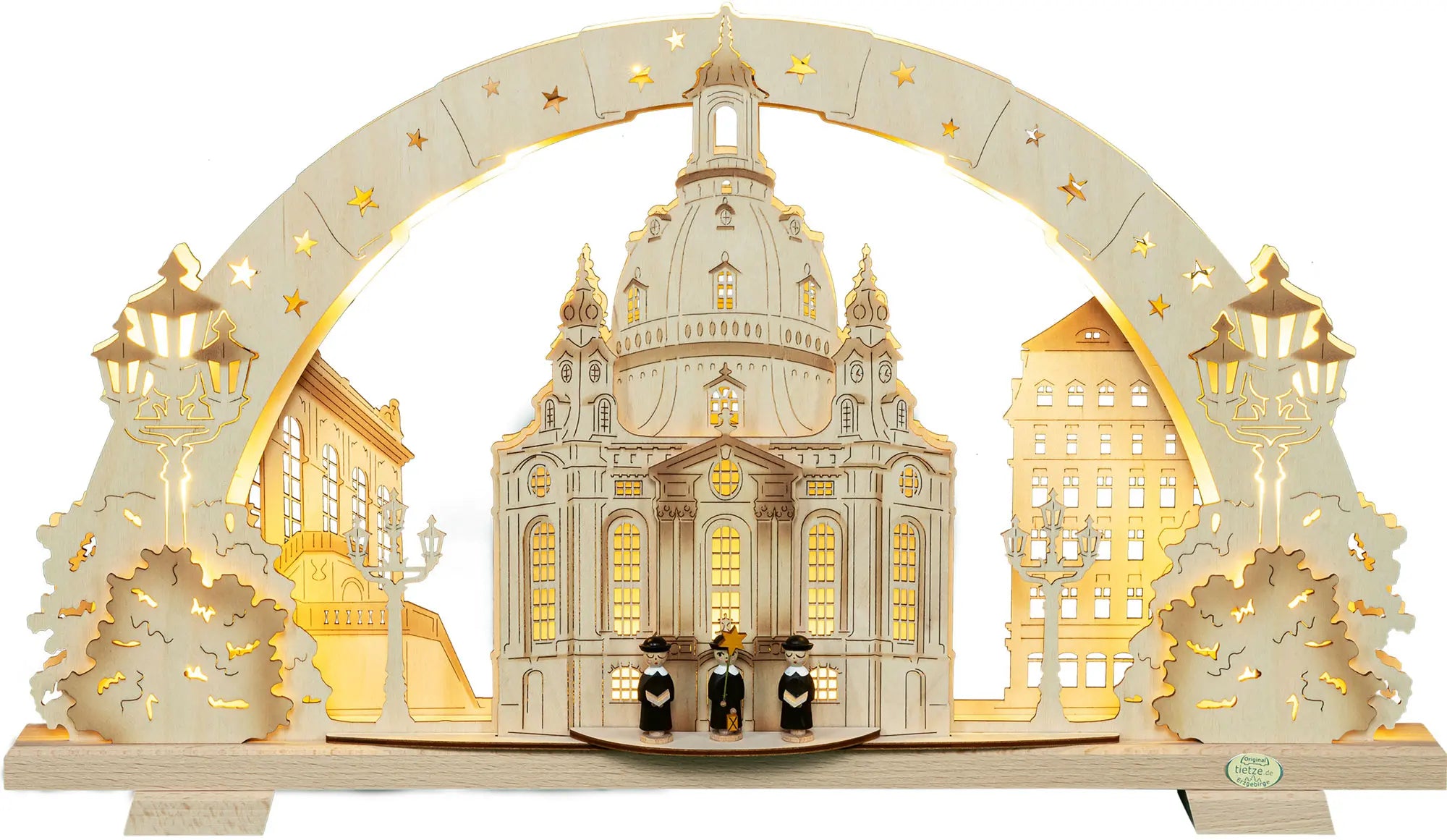 LED‑beleuchteter Schwibbogen mit Motiv der Dresdener Frauenkirche: In der Mitte steht die detailreich dargestellte Frauenkirche mit großer Kuppel und beleuchteten Fenstern. Daneben sind weitere Gebäude, Laternen und Bäume aus hellem Holz angeordnet. Unter dem Bogen stehen drei Kurrendefiguren mit Sternen. Der bogenförmige Rahmen ist mit Sternausschnitten verziert und wird von warmem, gelbem LED‑Licht indirekt beleuchtet. – Frontalansicht und beleuchtet